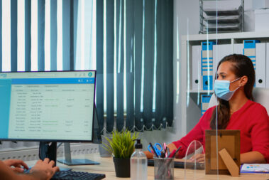 People wearing face masks back at work in office with new normal. Team working in workspace in personal corporate company typing on computer keyboard looking at desktop respecting social distancing.